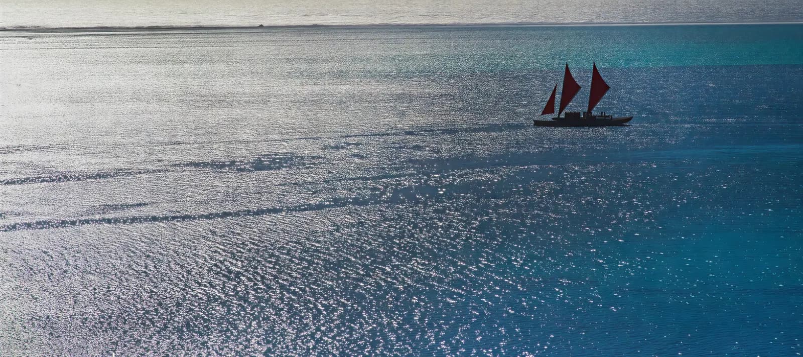 A voyaging waka with red sails alone on a glittering blue sea